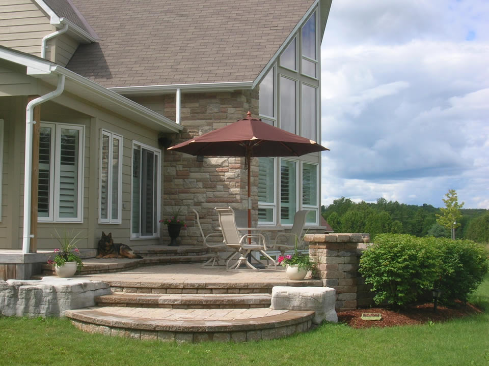 Raised patio with pillars and natural stone and burning bush hedge